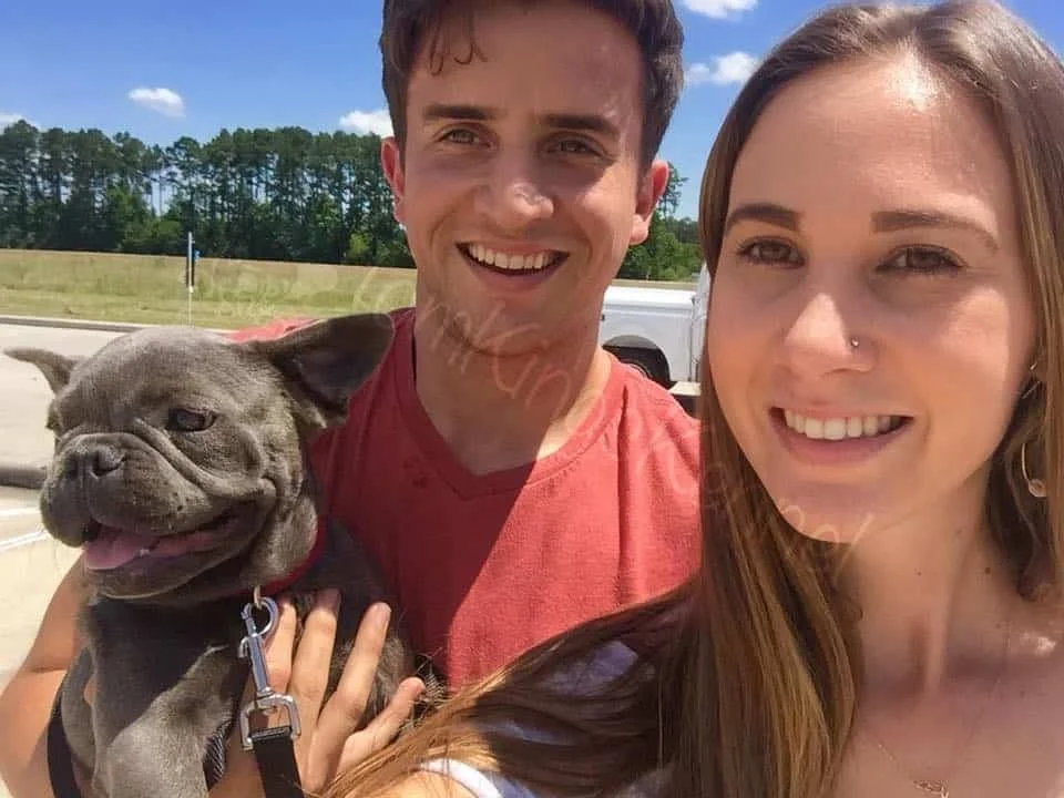 Couple taking a selfie outdoors while holding a grey French Bulldog puppy