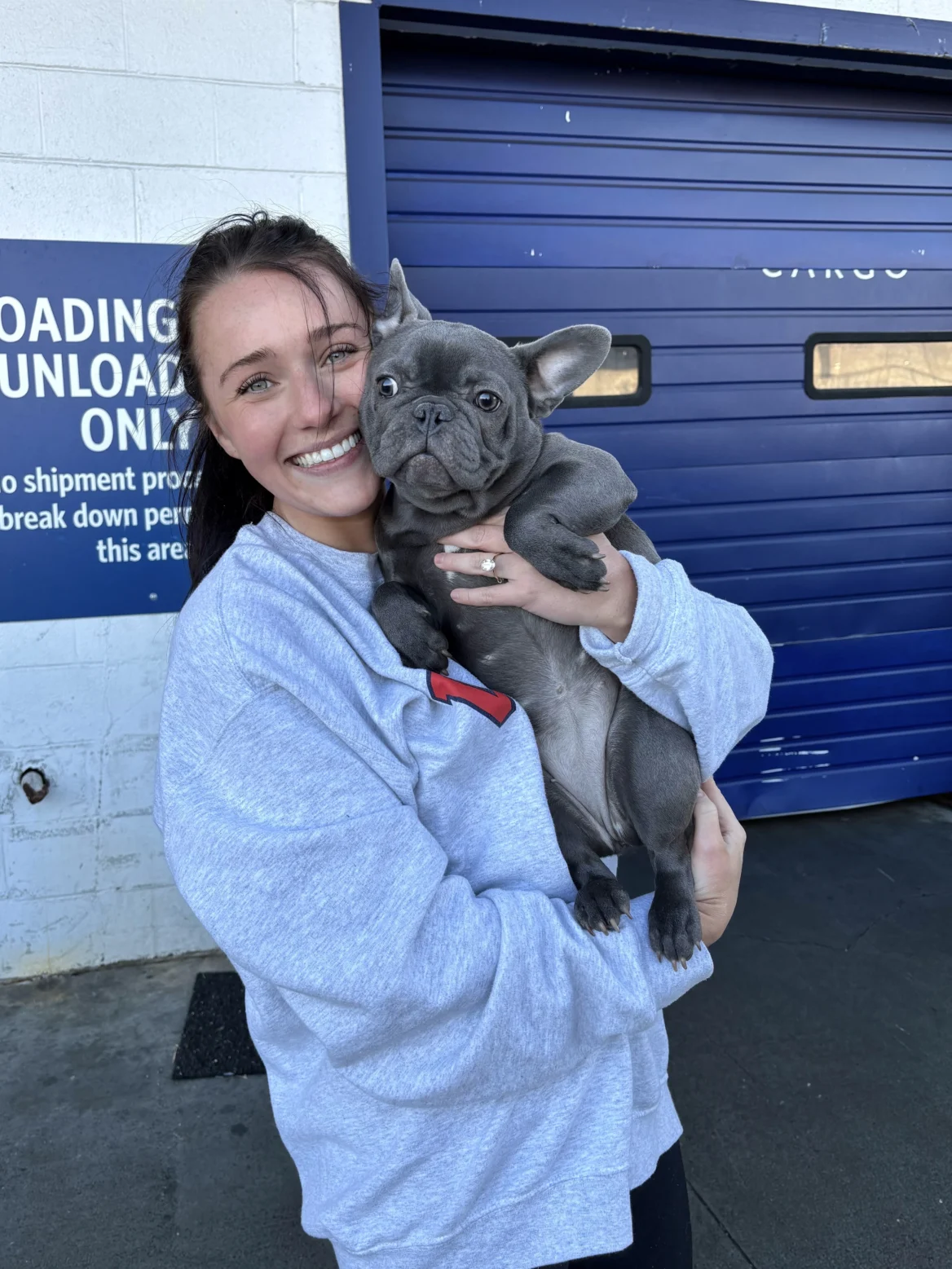 Woman holding a blue French Bulldog puppy outside a loading dock