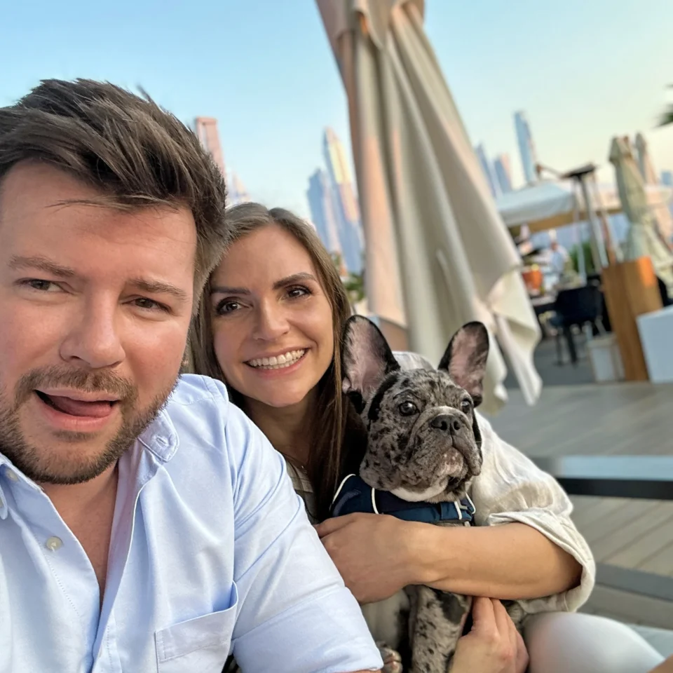 Couple taking a selfie with their merle French Bulldog on a rooftop terrace